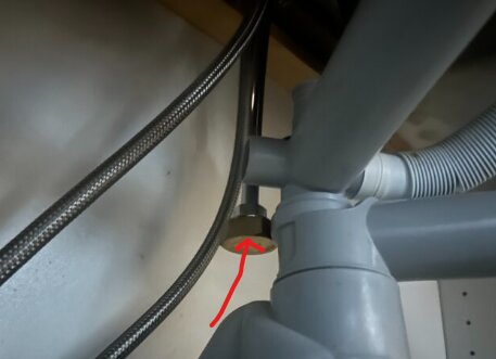 Bilden visar rör under diskbänken där en röd pil pekar på ett vred på en blandare.