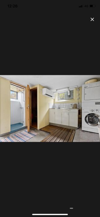 Tvättstuga med vit tvättmaskin och torktumlare, vitt skåp och ett litet fönster ovanför arbetsbänk.