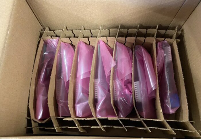 Nya reläkort för Nibe värmepumpar i kartong, täckta med rosa plastpåsar och avdelade med kartongsektioner.