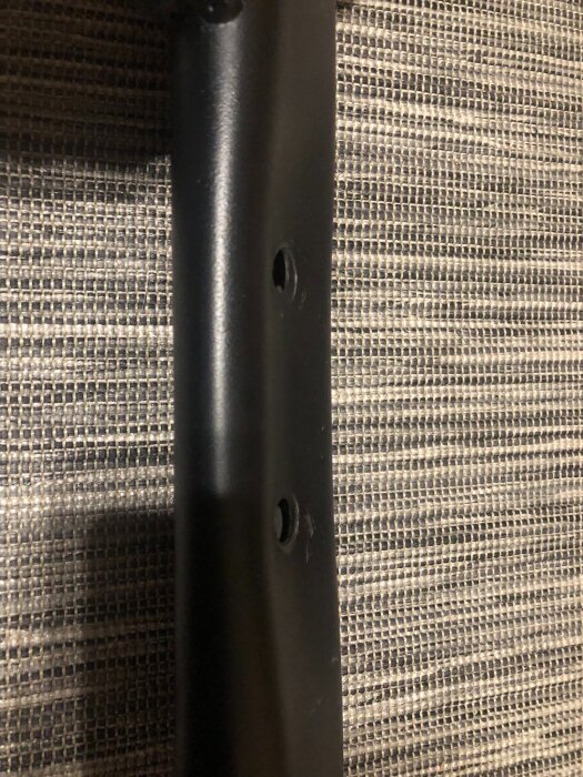 Svart metallstång med två defekta skruvhål från för hårt åtdragna skruvar, på en hopfällbar träningsbänk från Gorilla Sports.