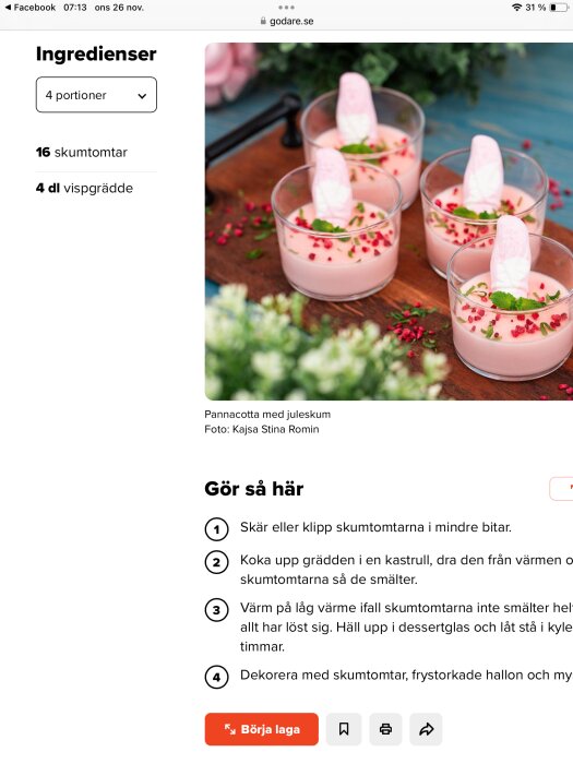 Fyra glas med rosa pannacotta dekorerad med skumtomtar, hallon och örter, på en träbricka.