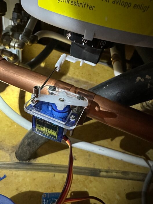 Termostatvred på varmvattenberedare modifierad med servo, stötstång och roderhorn för temperaturjustering, monterad på kopparrör.