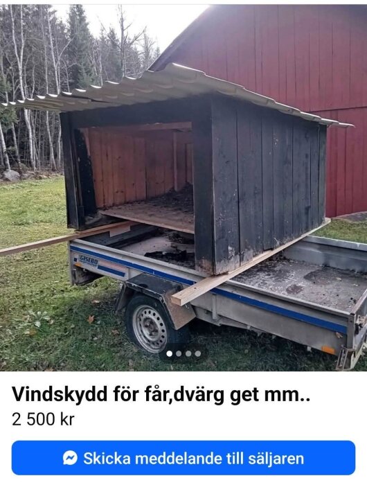 Vindskydd för djur placerat på en släpvagn, bakgrund med gräs och rödmålad byggnad.