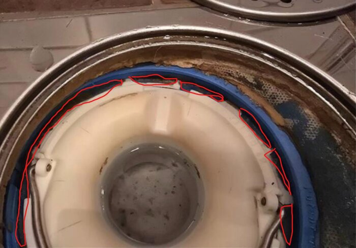 Tätskiktet runt ett vitt avloppsrör som sticker fram från ett golv, omgiven av en metallring och några till synes smutsiga ytor.