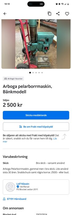En gammal men välbevarad Arboga pelarborrmaskin, bänkmodell, står på ett golv tillsammans med en röd pirra.