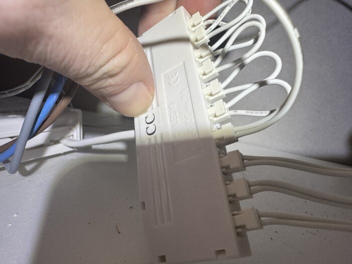 En hand håller i en vit kopplingsbox med flera anslutna vita kablar, där några kablar syns vara löst kopplade.