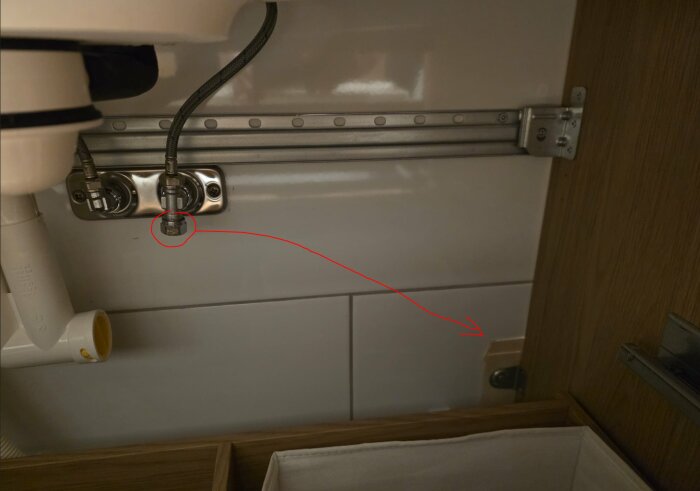 Vattenkoppling under ett handfat med en markerad rördragning och pil som pekar mot en plats bredvid ett skåp, potentiellt för en toalettdusch.