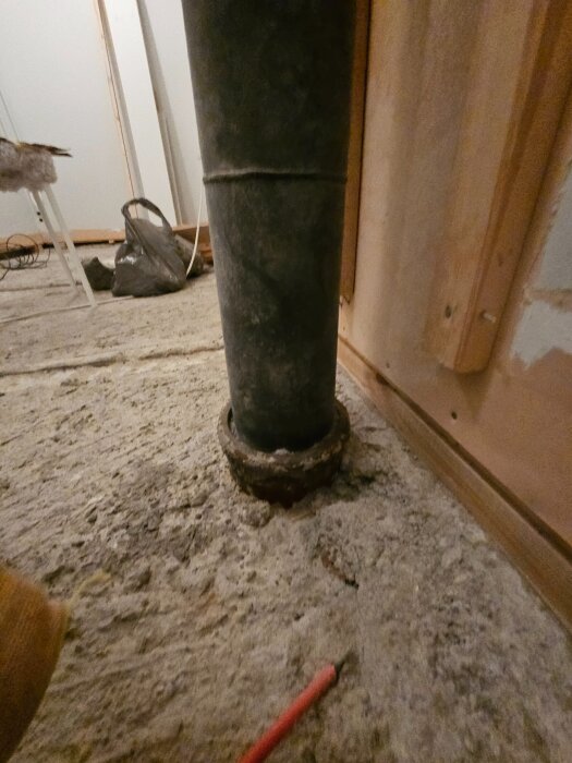 Gjutjärnsrör i golv efter att slits rivits bort, omgiven av trä och spånskivor i renoveringsprojekt. Frågor om ventilation och lukt diskuteras.