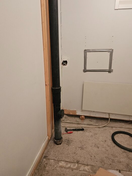 Svart rör vid vägg och tak som tidigare varit dolt. Betonggolv synligt med verktyg bredvid. Planer på att bygga ventilerat golv runt röret.