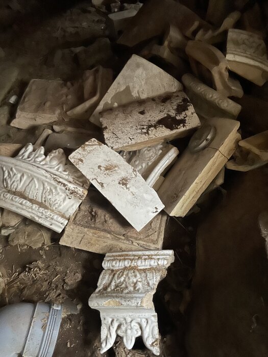 Trasiga vita och brunfärgade dekorativa gipsdetaljer och byggmaterial i en hög, med två särade bitar längst fram.