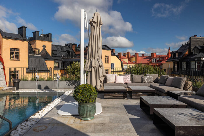 Takvåning med sittgrupp, parasoll och pool mot bakgrund av charmiga byggnader vid Karlaplan under en solig himmel.