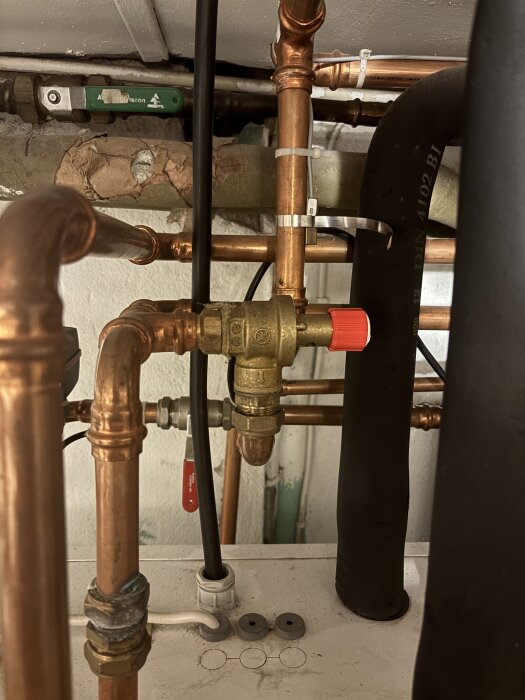 Rörsystem med kopparrör och ventiler, där fokus ligger på en del med invändig och utvändig gänga, samt en röd ventil och isolering.