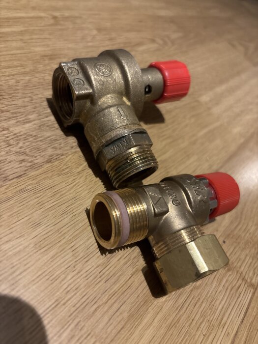 Två mässingsventiler på träyta, den ena med invändig och den andra med utvändig gänga, röd lock synlig.