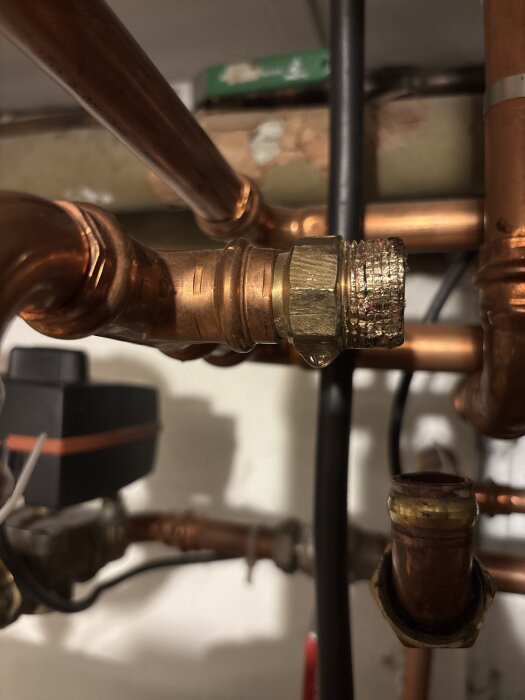 En kopparrörskoppling med skador från användning av en rörtång, omgiven av andra rör och anslutningar i ett trångt utrymme.