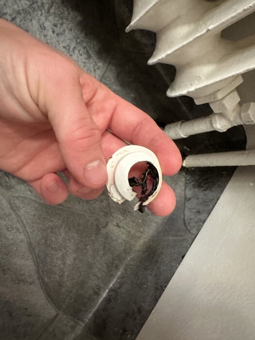 Hand som håller en vit, trasig rörmanschett med klibbig svart substans, bredvid ett element i ett badrum.