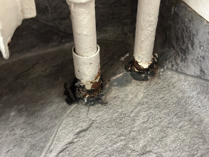 Närbild av våtrumsmatta med spricka mellan två rörgenomföringar och mörk massa runt rören.