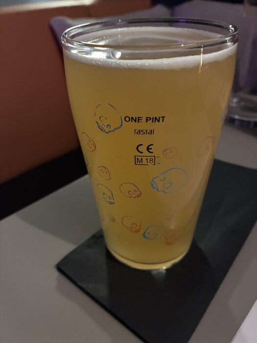 Ett glas med kall fatöl placerat på ett mörkt underlägg. Glaset är dekorerat med små skallar och markerat med "One Pint".