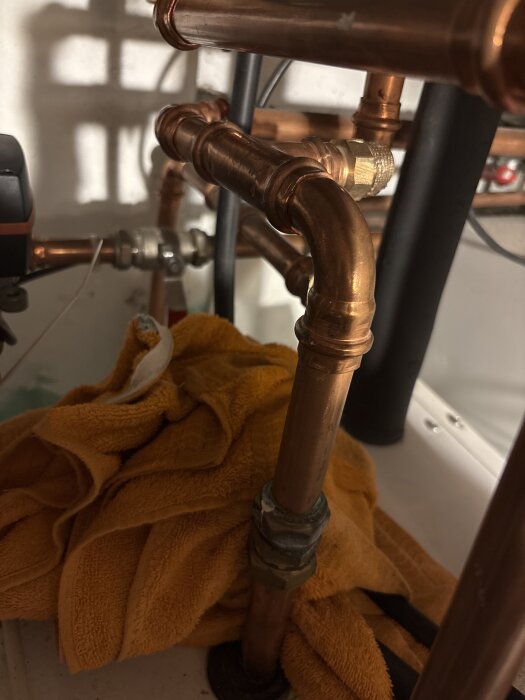 Kopparrör och kopplingar under ett projekt med orange trasa i bakgrunden.