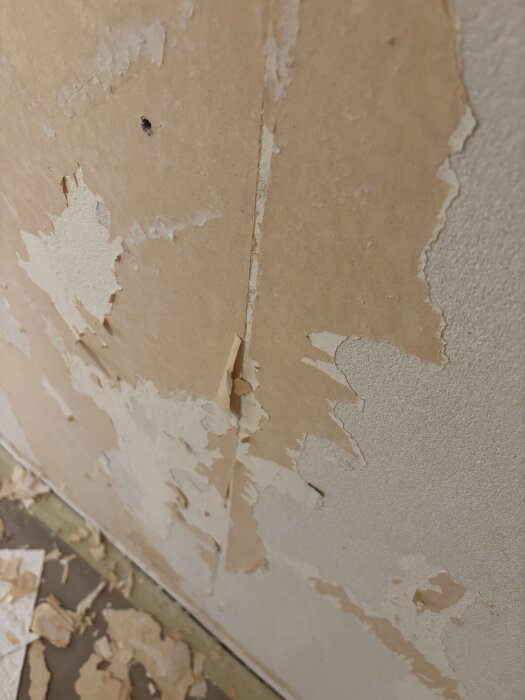 Nedriven tapet med kvarvarande pappersrester på en vägg, före spackling och målning i ett renoveringsprojekt.