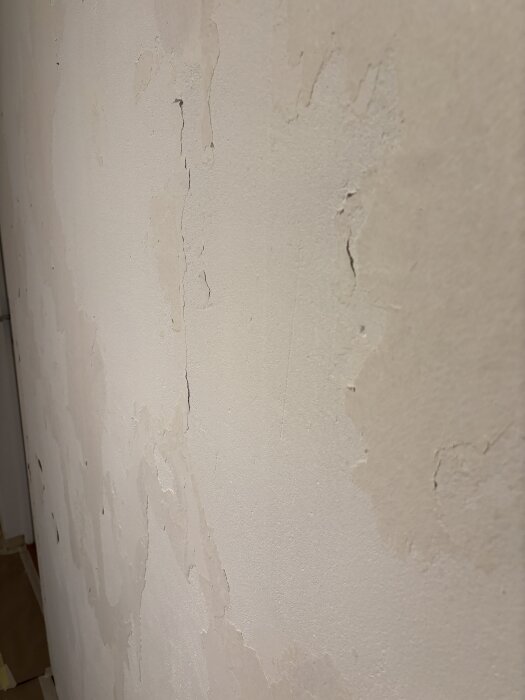 Vägg med rester av rivna tapetrester och ojämn yta, visas innan bredspackling, efter att primer applicerats.