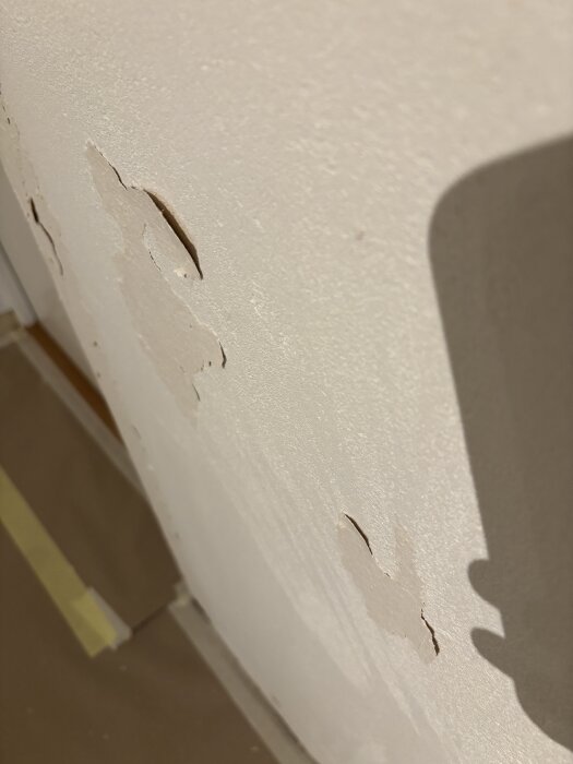 Vägg med avskalad tapet och ojämna ytor, synliga rester kvar efter borttagning, efter applicering av primer.