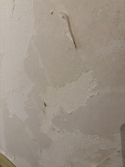 Vägg med borttagen tapet visar rester av papper och ojämn yta, där vissa delar av betongen är synliga och saknar primer.