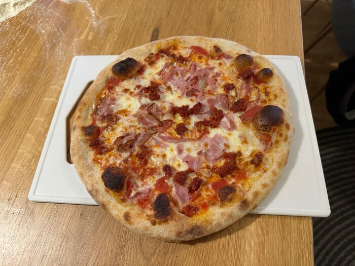 Hemlagad pizza med skinka och tomatsås på en träyta.
