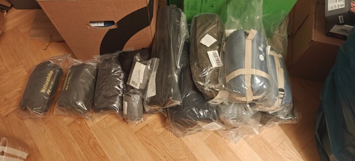 Paket med Naturehike-produkter uppställda på ett parkettgolv, flera inslagna i genomskinliga plastpåsar bredvid en kartong.