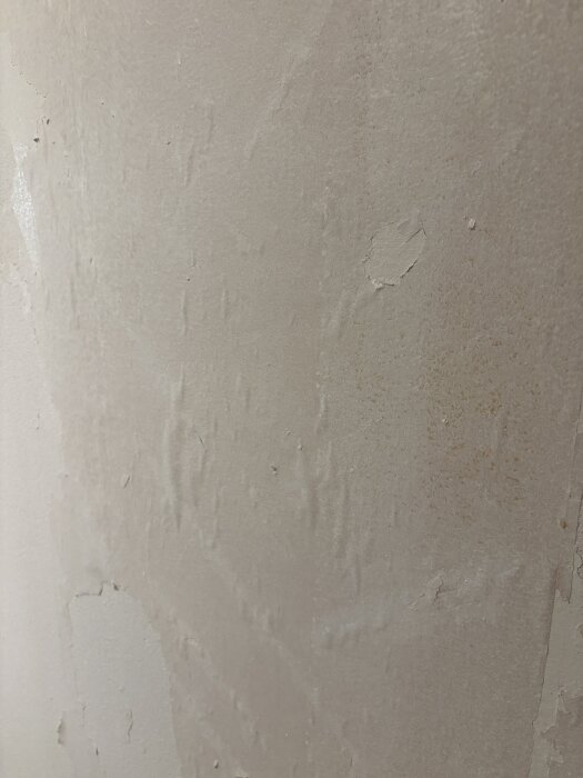 Bubblig yta av papp under ett lager primer på en vägg, vilket visas som ojämnheter och skador på ytan.