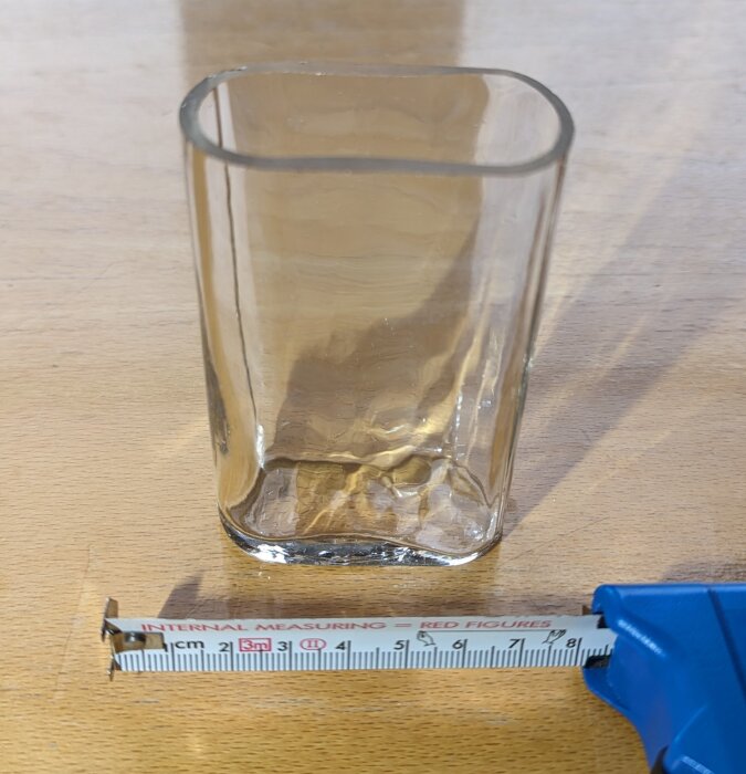 Ovalt glas bredvid måttband på träbord, del av gamla fönsterset.