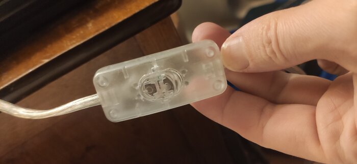 Genomskinlig strömbrytare av plast med en elektrisk kabel, hålls i en hand där innehållet syns genom skalet.