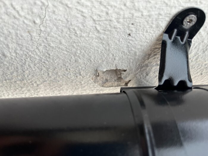 Märke på vit, grov fasad intill ny svart hängränneinfästning.