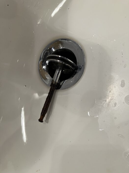 Rostig metallskruv i bottenpluggen på ett porslinstvättställ i badrummet.