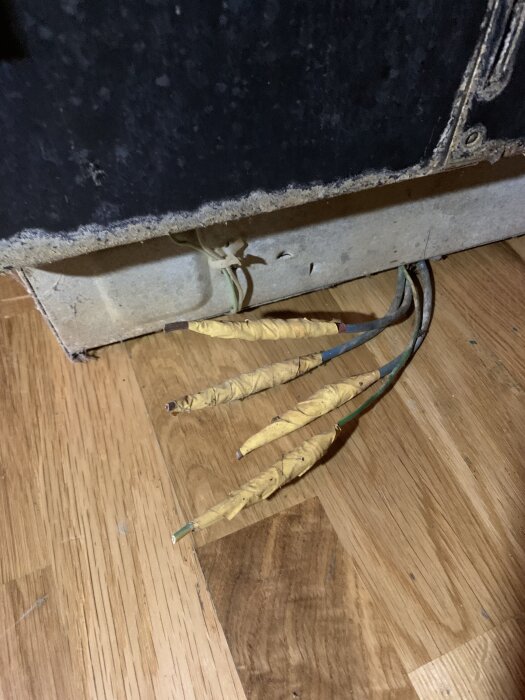 Baksida av ett gammalt bastuaggregat med exponerade elkablar, monterat på trägolv.