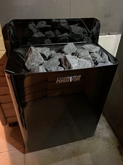 Svart Harvia bastuaggregat med stenar ovanpå, placerat i ett hörn av bastun.
