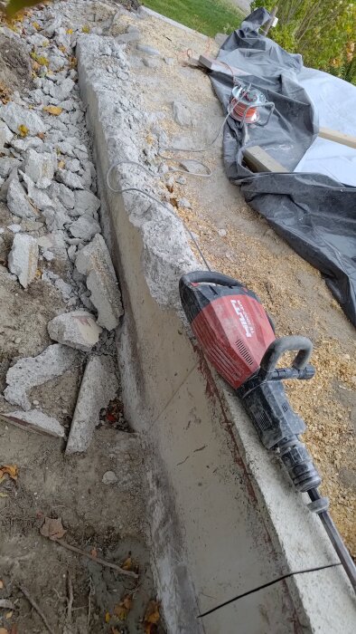 Betongvägg och bitar av nedbruten cement vid en rivning, med en stor borrmaskin och sågspån spridda på marken.