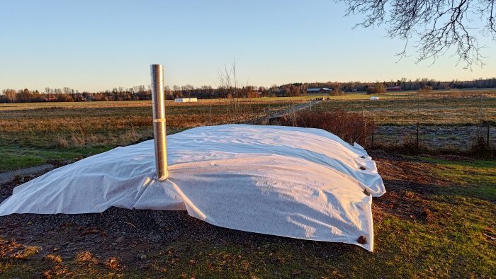 Täckta jordhögar med rör och platon ovanpå en byggplats, omgivna av öppet landskap under klar himmel.