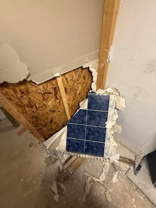 Rivet badrum med trasiga väggar, synliga reglar och blå kakelrester ovanpå osb-skiva.