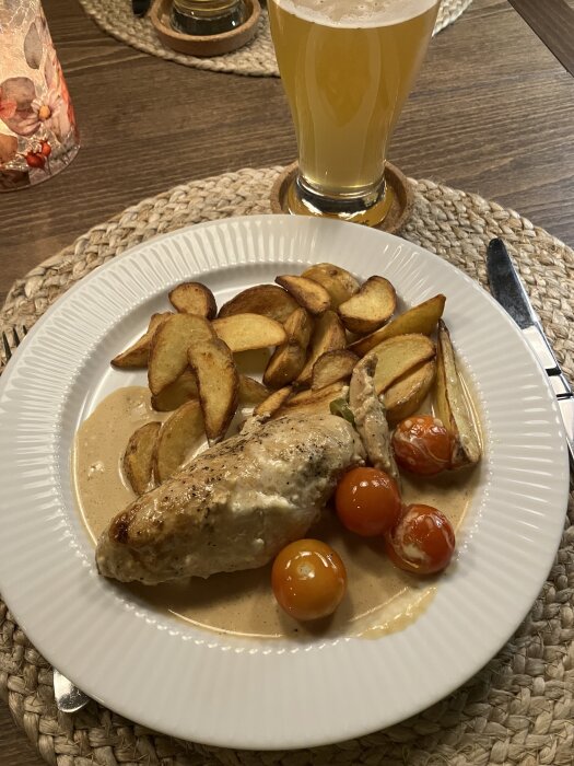Kycklingfilé i whiskysås med klyftpotatis och tomater på en tallrik, serveras med ett glas ljus öl.