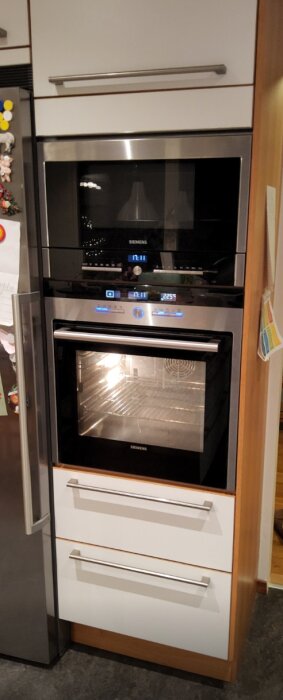 Högskåp med inbyggd ugn och micro, två lådor under ugnen. Siemens apparater, kök med vit och träfärgad design.