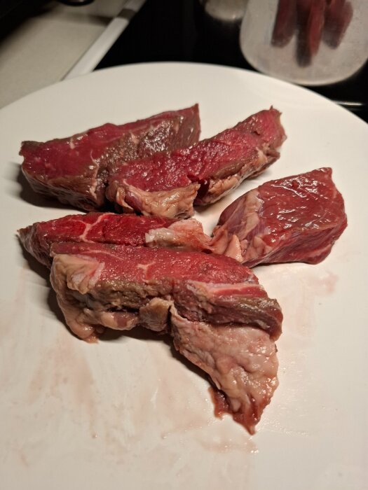Rå entrecote köttbitar ligger på en vit tallrik.