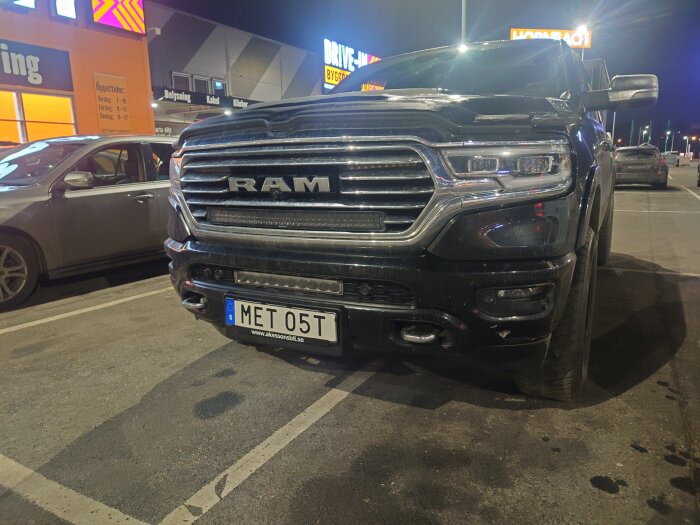 Svart RAM-bil parkerad på en upplyst parkeringsplats med registreringsskylt "MET 05T" synlig.