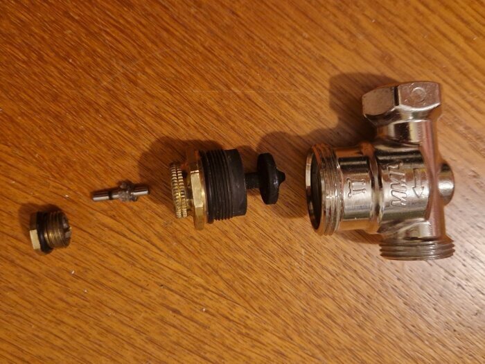 Delar av en radiatorventil på ett bord, från vänster till höger: packbox med stift, ventilinsats med kägla, och ventilhus.