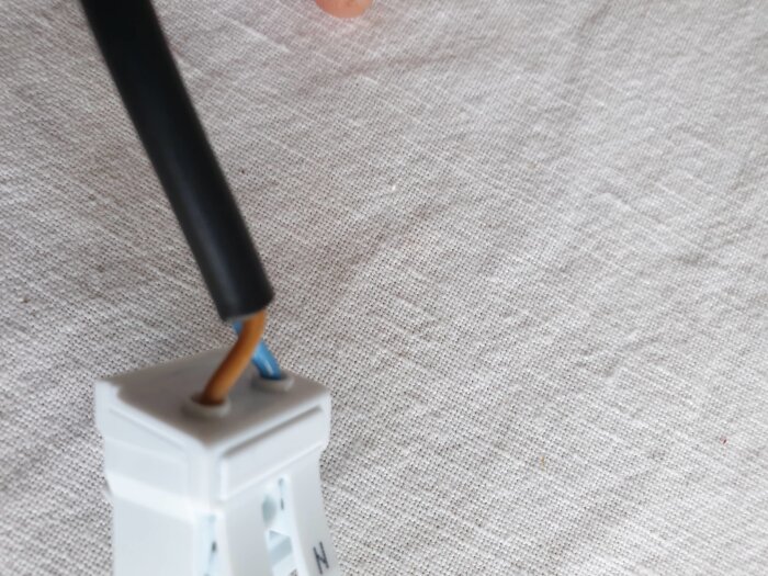 Två elsladdar, brun och blå, som är inkopplade i en vit kopplingsplint på ett tygunderlag.