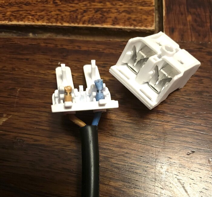 Elektrisk kontakt där sladdar är anslutna till en del, med den andra delen av kontakten liggande bredvid, på ett trägolv.