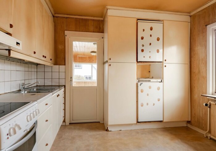 Gammalt kök med vit kakel, diskbänk och slitna skåp i ett hus från 1945, potentiellt riskområde för asbest vid renovering.