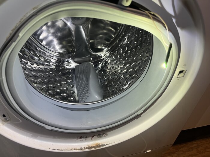 Öppen tvättmaskin med trumma i rostfritt stål, med synlig sladd och led-belysning inuti.