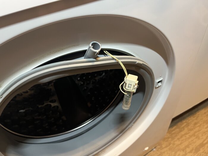 Närbild av en tvättmaskinsöppning med en lös anslutning och ledningsdetaljer vid dörren.