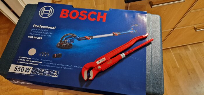 Kartong för Bosch GTR 55-225 slipmaskin och en röd rörtång ligger på en trälåda.