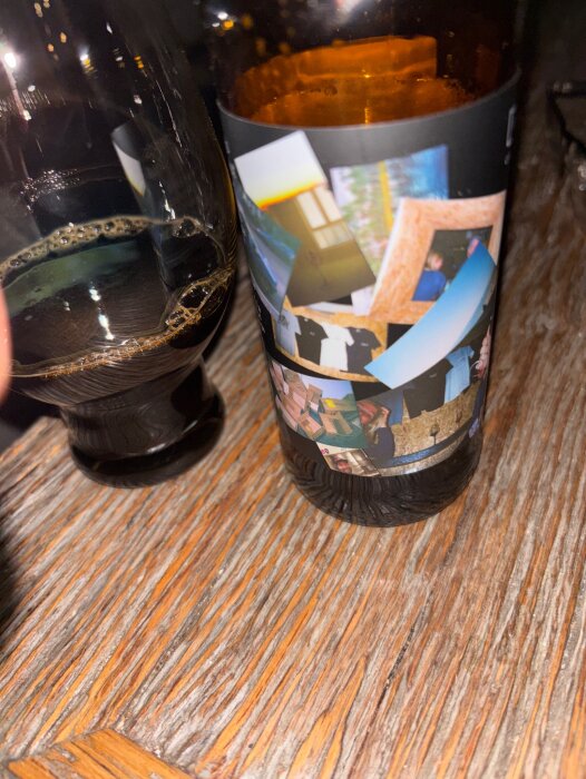 Flaska med öl på träbord, etikett med collage av bilder, bredvid ett glas med mörk öl.
